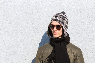 Wall Mural - Stylish male teenager. Handsome young man in sunglasses and knitted hat poses outdoors on cold sunny winter day