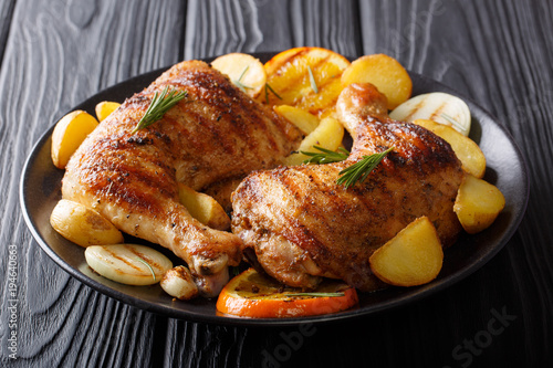Fotografía Hot fried chicken legs with grilled oranges, lemon, onion, garlic and potatoes close-up