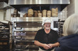 © Maskot - Smiling senior male baker standing against cooling rack at bakery