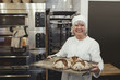 © Maskot - Smiling baker holding fresh baked breads in tray at bakery