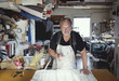 © Maskot - Portrait of senior male owner standing with fabric at workbench in workshop