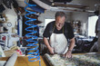 © Maskot - Senior male owner cutting fabric at workbench in workshop