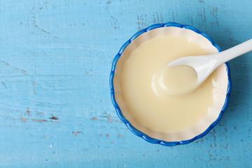 condensed milk or evaporated milk in bowl on blue table top view.