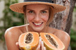 © WHstudio Leushin N - Horizontal portrait of glad lovely woman poses naked, wears summer hat, holds organic exotic papaya, supports healthy eatting. Beautiful female likes tropical fruits, spends summer at hot country.