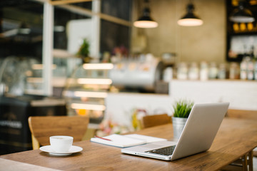 Open laptop computer with space for your brand lying on a wooden table in modern cafe bar interior, portable net-book and cup of hot drink, electronic distance work via internet during coffee break