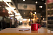 A red cup on wooden table and blurry light in background.
