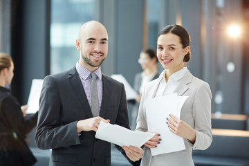 Canvas Print - Two young smiling brokers with contracts looking at camera during negotiation