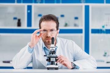 Wall Mural - portrait of scientist in white coat and eyeglasses with microscope in laboratory