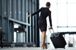 © pressmaster - Back view of elegant businesswoman in suit and high-heeled shoes pushing her suitcase before her in airport
