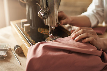 Sewing keeps my mind relaxed. Cropped shot of female tailor working on new project, making clothes with sewing machine in workshop, being busy. Young designer making her ideas come true