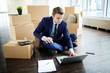 © pressmaster - Busy young manager in suit sitting on the floor of new office among boxes and browsing in the net