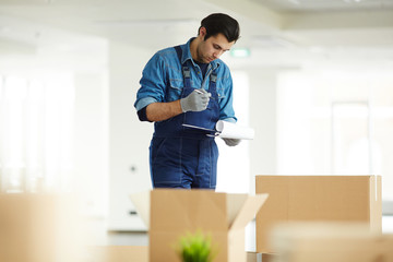 Wall Mural - Young courier in uniform checking signature of client in receiving document over open box