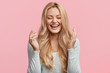 Leinwandbild Motiv Isolated shot of joyful blonde young cute woman laughs joyfully as hears funny anecdote from friend, has long light hair, poses against pink studio wall. Happiness and positive emotions concept