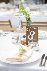 Simple but luxury rich table setting for a wedding celebration in nice cozy restaurant. Wineglasses, plates and bouquet of summer seasonal flowers on a table. Sunlight from a window. Copy space