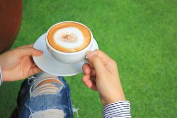 Woman hands holding hot cups of coffee with milk foam on green background with copy space