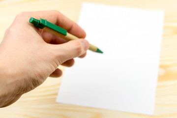 Hand holds pen on  wooden background with sheet of white paper