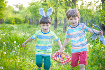 Kids on Easter egg hunt in blooming spring garden. Children searching for colorful eggs in flower meadow. Toddler boy and his brother friend kid boy play outdoors