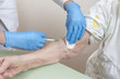 Pielęgniarka w rękawiczkach jednorazowych dezynfekuje miejsce na ręce starej kobiety przed pobraniem krwi.