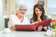 © Bojan - Cheerful grandmother and granddaughter looking at family photo album at home.