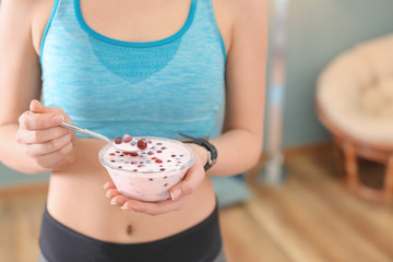 Sporty young woman eating yogurt with berries after fitness training at home