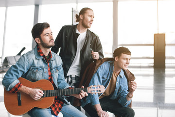 Wall Mural - Cheerful friends performing melody while waiting for plane. Friendship and entertainment concept