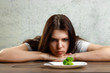 © Aliaksandr Marko - sad young brunette woman dealing with anorexia nervosa or bulimia having small green vegetable on plate. Dieting problems, eating disorder.