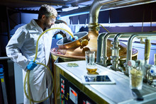 Confident Middle-aged Worker Of Modern Brewing Plant Wearing White Coat And Protective Goggles Using Horse While Washing Cylindrical Beer Maturation Tank