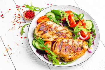 Grilled chicken breast. Fried chicken fillet and fresh vegetable salad of tomatoes, cucumbers and arugula leaves. Chicken meat salad. Healthy food. Flat lay. Top view. White background