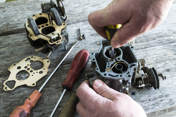 The man is repairing the carburetor of the car.