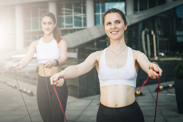 Summer day. Two young women athletes jumping on skipping ropes in city street. Girls train outdoors. Workout, sports, healthy lifestyle. In background is modern glass building. Film effect.