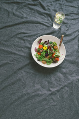 Poster - Healthy food concept. Summer salad with vegetables and flowers nasturtium and violets on bed with glasses of water with lemon, top view