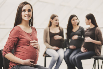 Wall Mural - Beautiful pregnant woman is looking at the camera. Happy pregnant women are talking together at antenatal class at the hospital on background