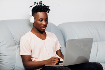 Wall Mural - African American man sitting with laptop on sofa