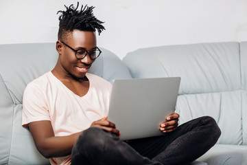 Wall Mural - African American man sitting with laptop on sofa