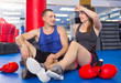 Female boxer is sitting with man and talking about healthy in gym.