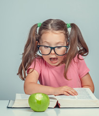 Wall Mural - curious beautiful cute little girl next to thick book and green apple