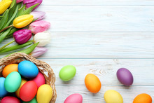 Colorful Easter Eggs In Basket With Tulips On Wooden Table