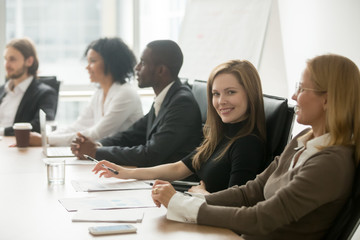 Sticker - Young smiling businesswoman looking at camera at corporate group meeting, business training participant sitting at conference table with diverse colleagues, company manager portrait at team briefing