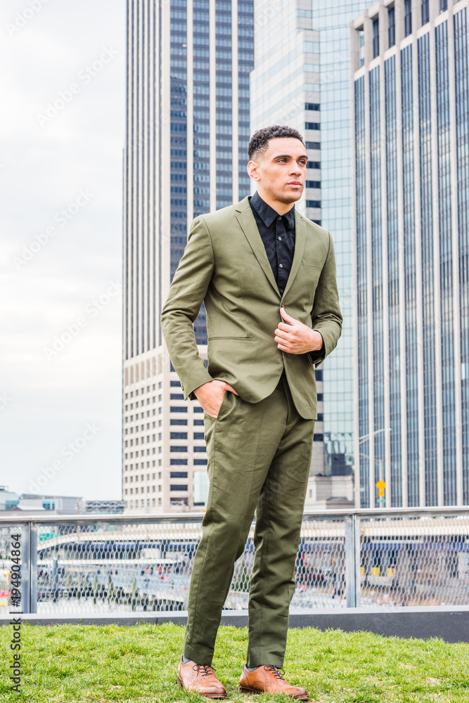 Photo Stock Young handsome American Businessman traveling in New York,  wearing green suit, black undershirt, brown leather shoes, standing in  front of business district with high buildings, looking forward