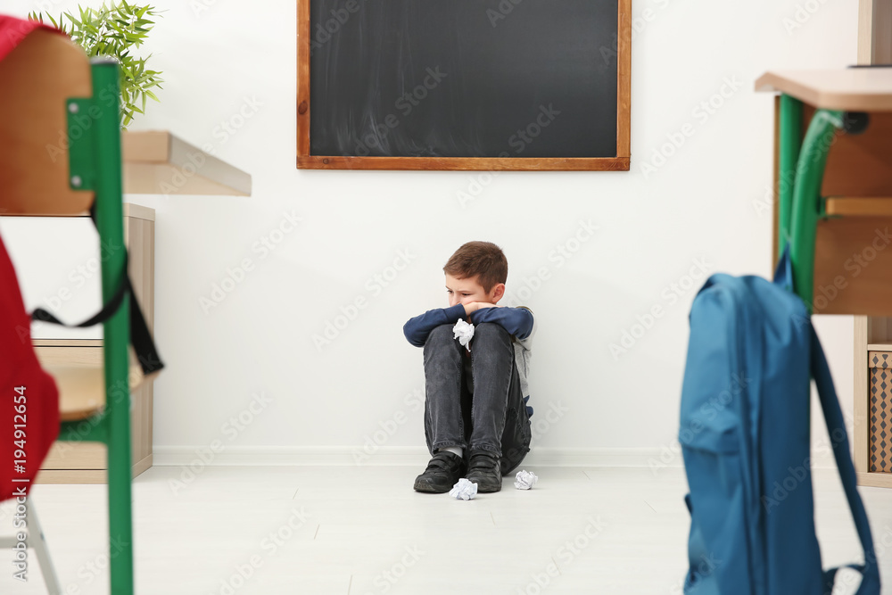 Sad little boy sitting on floor in classroom