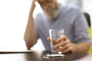 Canvas Print - Senior man with pills and glass of water at workplace