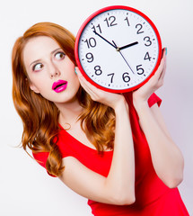Surprised redhead girl in red dress with big clock