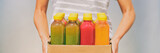 Woman holding delivery box of freshly cold pressed fruit and vegetable juice bottles. Trendy young person carrying organic raw juices. Juicing is a food trend for diet cleanse detox. Banner panorama.