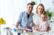 © LIGHTFIELD STUDIOS - Smiling family with daughter coloring Easter eggs