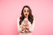 Surprised Woman With Red Lips Typing Text Message Or Scrolling Social Network Using Smartphone, Over Pink Background