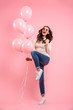 © Drobot Dean - Full length image of cheerful woman 20s in jeans clenching fists with delight while holding lots of air balloons in hand, isolated over pink background