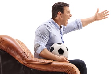 Canvas Print - Angry young man with a football sitting in an armchair and yelling