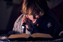 Boy Reading Book With Flashlight