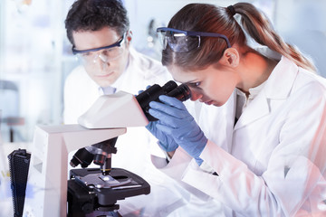 Poster - Life scientists researching in laboratory. Attractive female young scientist and her doctoral supervisor microscoping in their working environment. Healthcare and biotechnology.