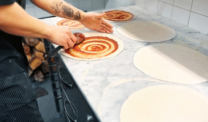 Wall Mural - cook applying tomato sauce to pizza at pizzeria